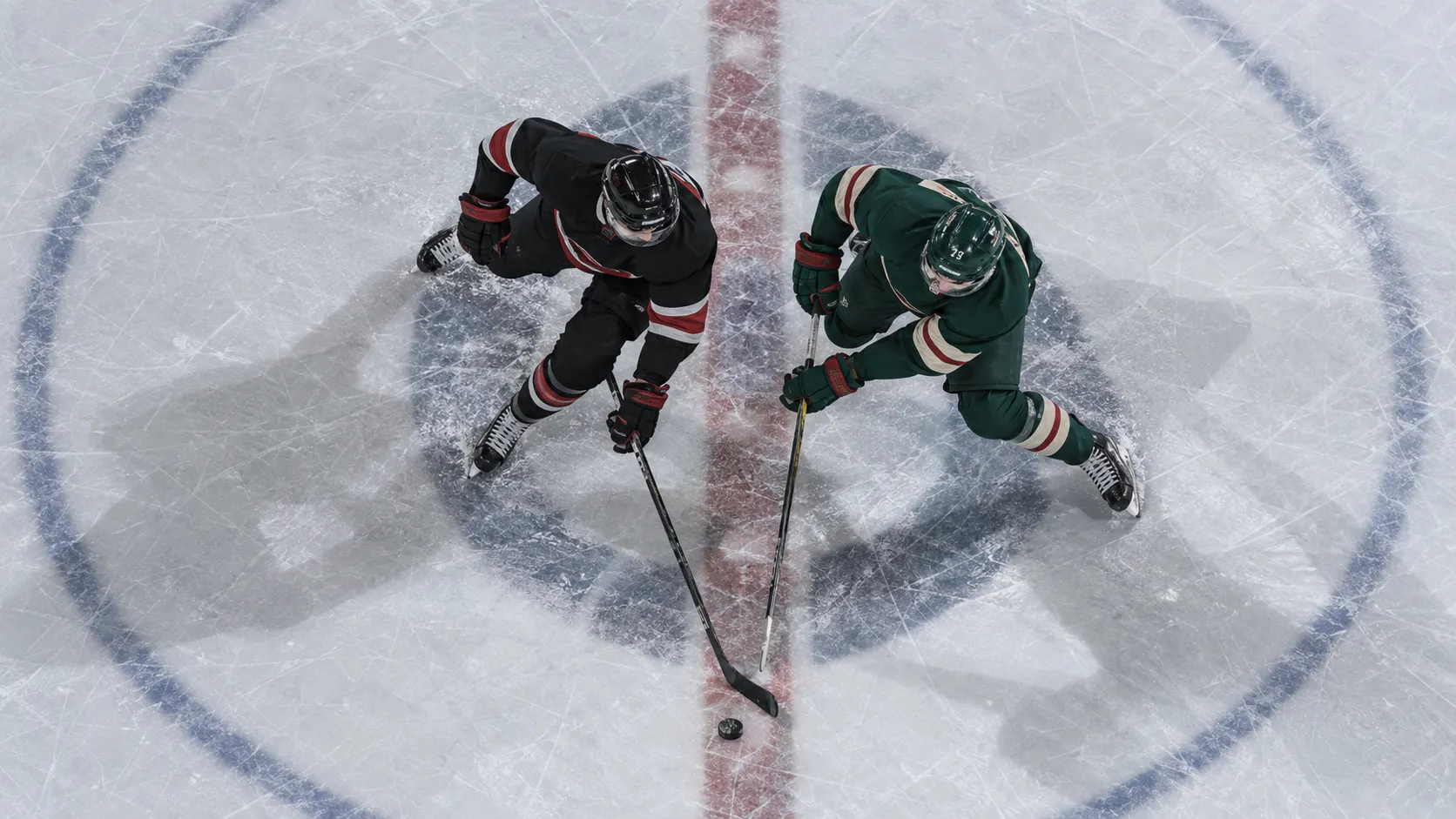 Overhead view of two hockey players in black and green uniforms competing for the puck at center ice