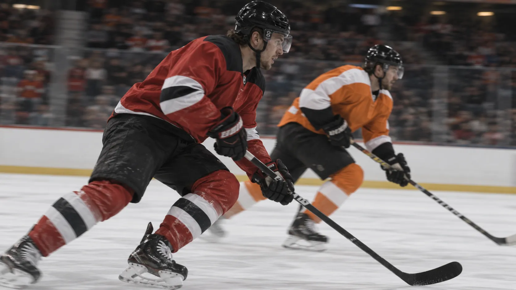 Side on view of two hockey players in Devils red and black and Flyers orange and white skating across the ice with the crowd blurred behind