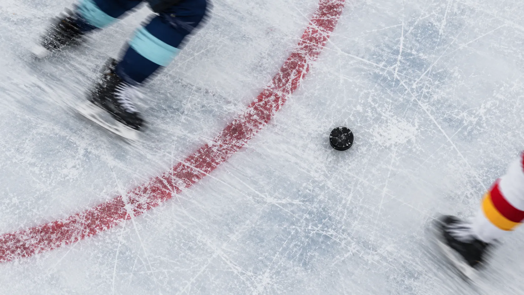 Overhead view of a puck on scratched ice  with blurred skates passing beside a red faceoff circle marking