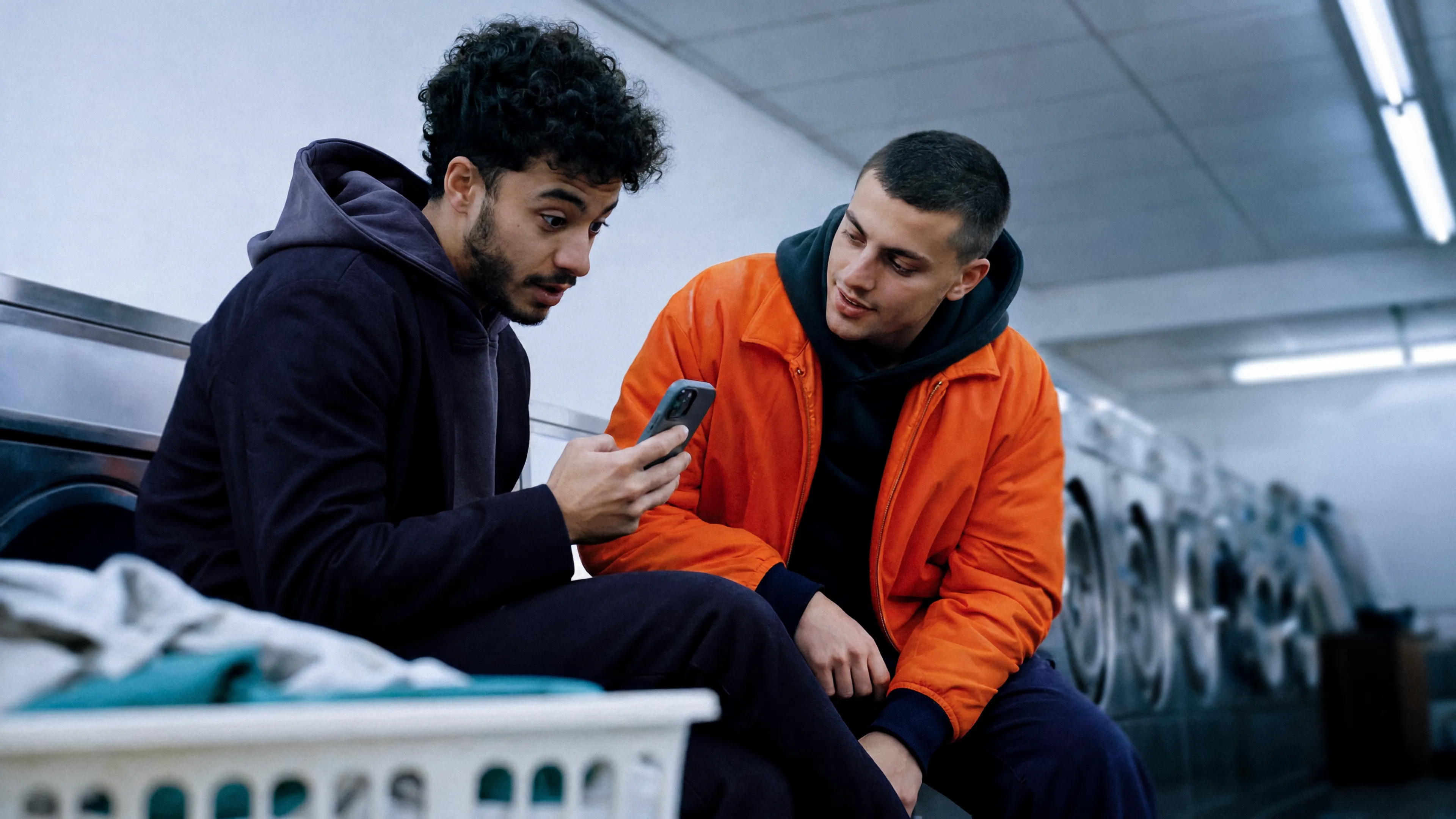 two men sitting at a laundromat looking at one man s phone