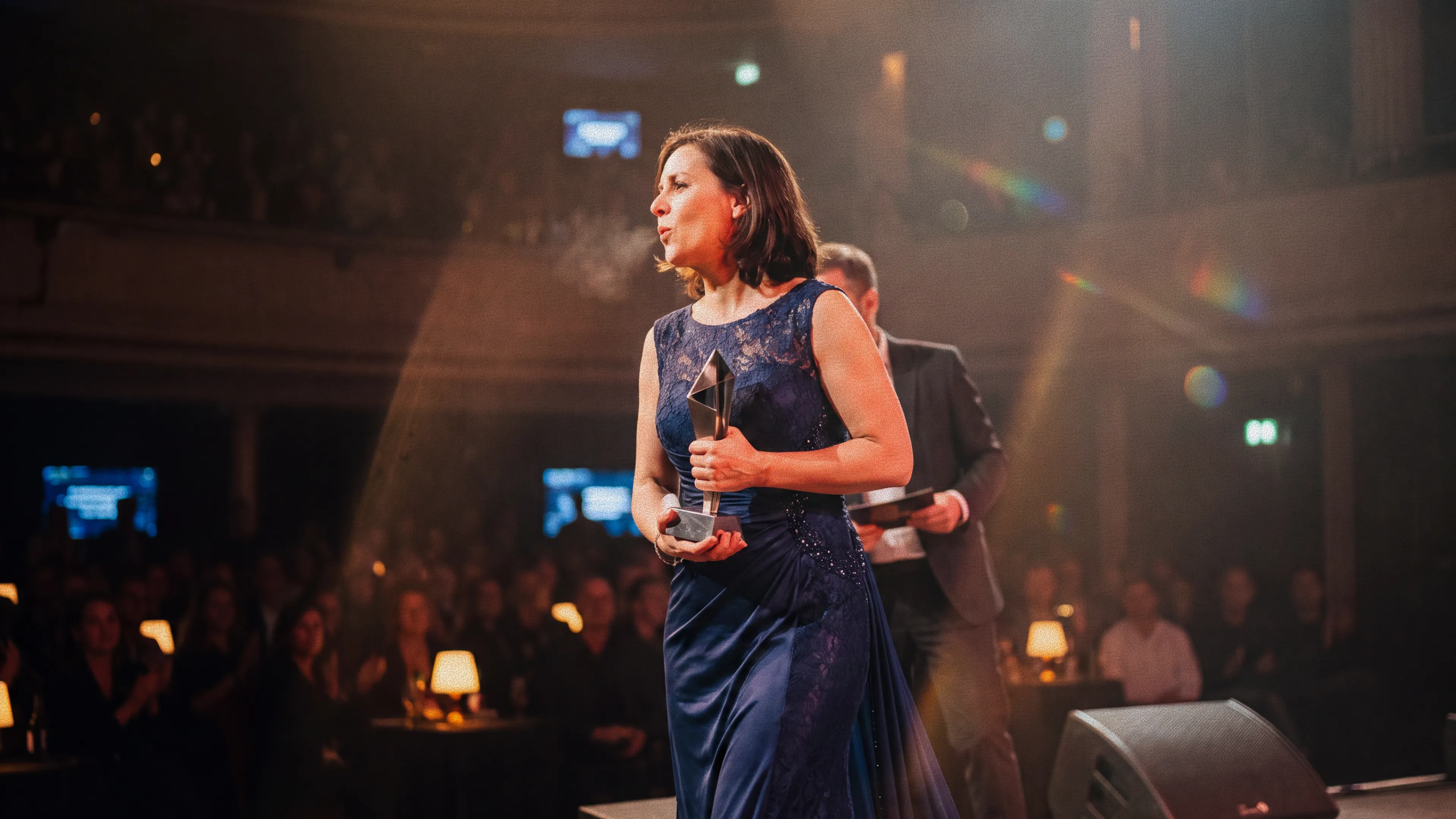 A woman on a scene under spotlight  holding an award