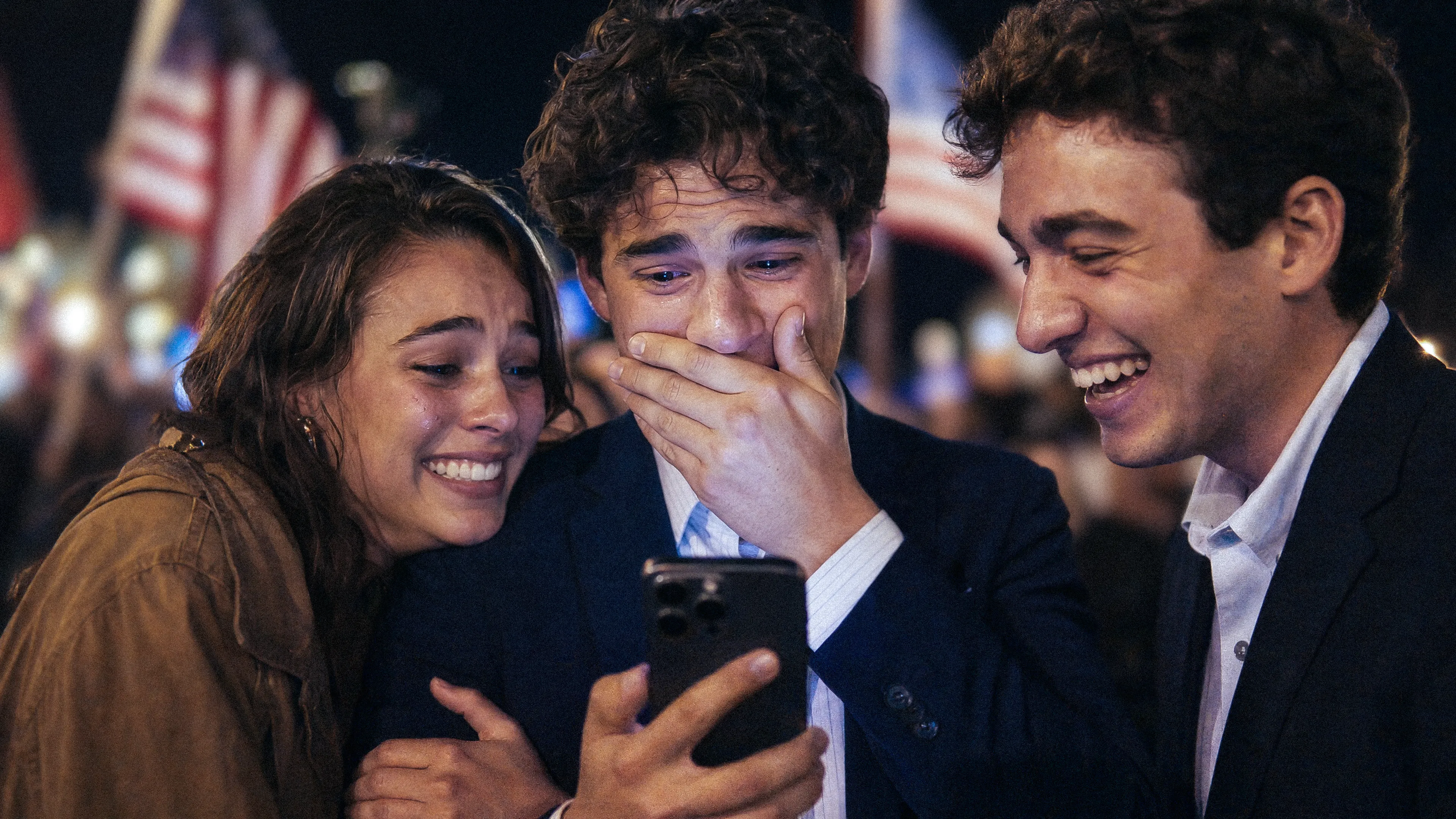 two men and one woman looking at one man s phone excited about what they see  they are at a political rally with American flags in the background